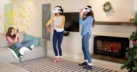 Friends wearing vr headsets playing holiday games in cozy living room by fireplace