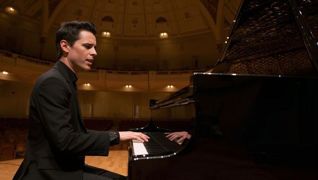 Young pianist playing grand piano on empty concert hall stage with dramatic lighting