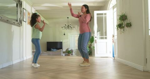 Mother and daughter singing and dancing in bright minimalist living room with plants