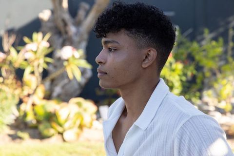 African american man profile standing in sunlit garden wearing white shirt with succulents