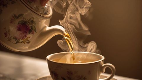 Vintage Floral China Teapot Pouring Amber Tea into Matching Gold-Rim Teacup with Curling Steam