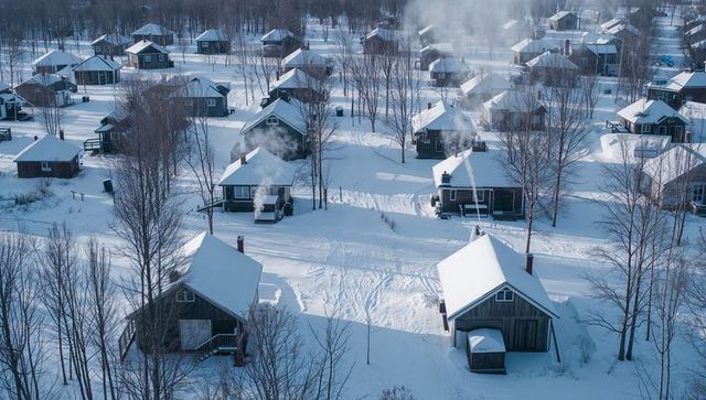 Aerial winter village of wooden cabins in deep snow with smoking chimneys and tracks