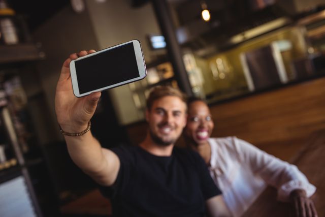 Happy couple taking selfie in cozy restaurant. Perfect for use in campaigns about social media, modern relationships, and casual dining experiences. Ideal for blogs, advertisements, and social media posts celebrating moments and memories.
