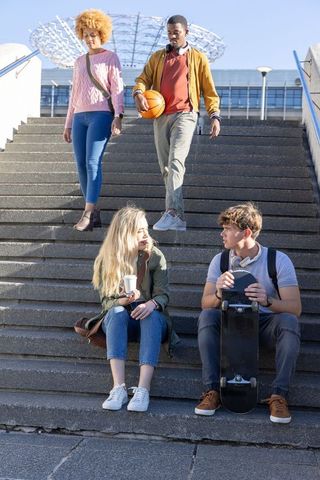 Diverse college friends hanging out on campus steps with skateboard and basketball
