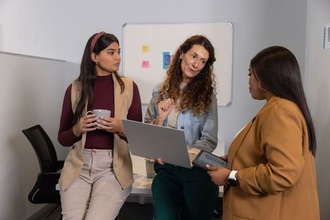 Three professional women collaborating in modern office during informal meeting with laptop