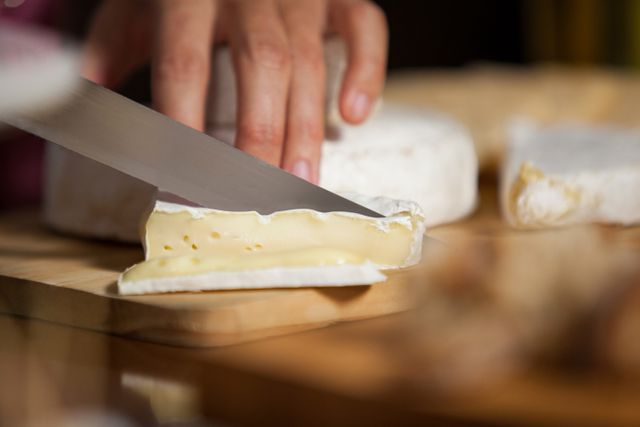 Hand of female staff cutting cheese at counter in market