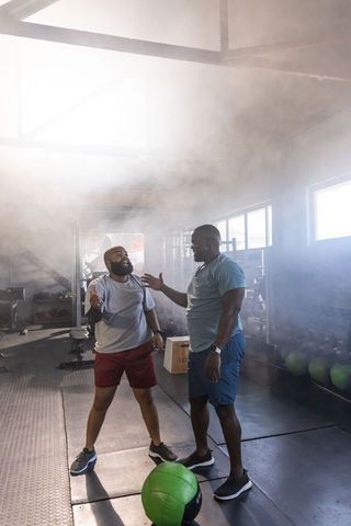 Two african men coaching and training together in backlit gym during functional workout