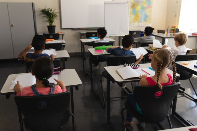 This image shows a group of children sitting at desks in a classroom, focused on their studies. Ideal for use in educational materials, school websites, and articles about education, learning environments, and classroom activities.