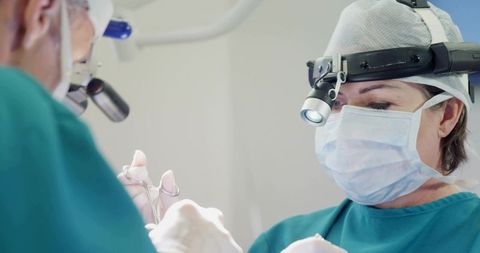 Female surgeon performing delicate surgery monitoring incision wearing surgical headlamp