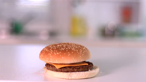 Slow Motion Burger Bun Falling on Cheeseburger in Kitchen