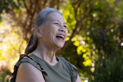Joyful senior asian woman laughing outdoors in sunlit garden with bokeh background
