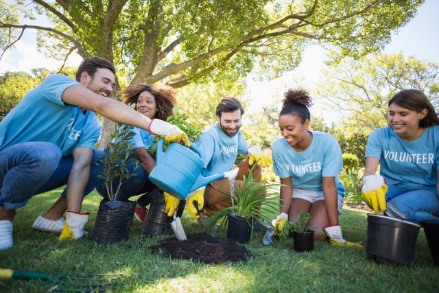 Group of diverse volunteers working together to plant trees in a park. They are wearing gloves and blue volunteer shirts, and seem engaged in the activity, fostering community spirit. This image is suitable for use in promotional materials for environmental campaigns, charity events, community building projects, and sustainable living articles.