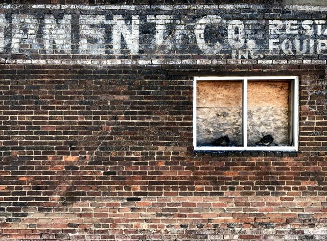 Weathered brick wall with faded vintage sign and boarded-up window. Perfect for themes related to urban exploration, historical architecture, and abstract art. Use it for backgrounds, posters, or adding a rustic feel to creative projects.