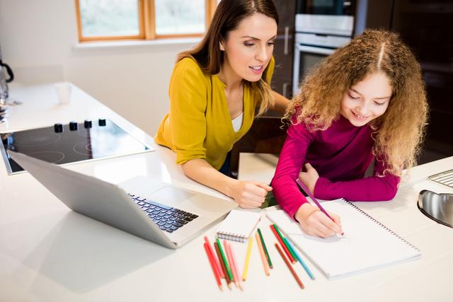 Mother helping daughter with homework in the kitchen. They are using a laptop, pencils, and notebook. This scene represents family bonding, education, learning at home, and parental support in children's studies. Suitable for promoting educational resources, homeschooling materials, family-oriented products, and articles about parenting and learning support.