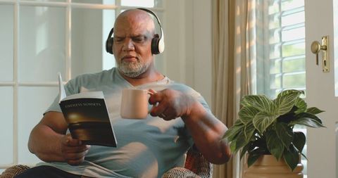 Senior Man Relaxing with Book and Headphones at Home