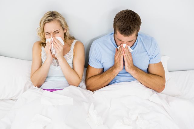 Couple covering nose while sneezing on bed in bedroom
