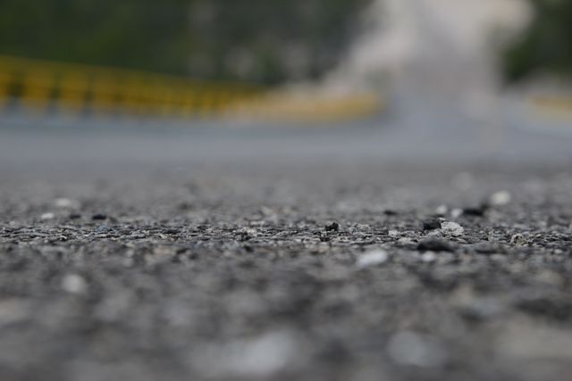 Close-up of asphalt road showing detailed texture with blurred background. Suitable for transportation projects, road construction themes, or as a background for presentations involving travel and infrastructure.