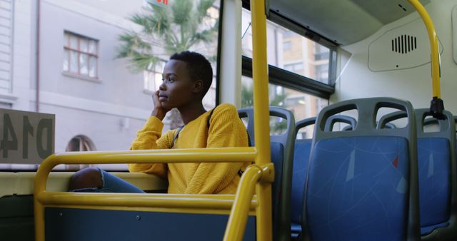 Image showing a young woman in a yellow sweater sitting alone on a city bus, looking pensive and lost in thought. Bright urban setting with a view of the city through the window. Ideal for illustrating concepts of solitude in a bustling city, commuting, public transportation, or introspective moments during travel.