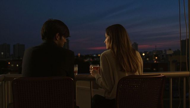 Rooftop couple sharing quiet sunset drinks, city skyline at dusk, intimate conversation