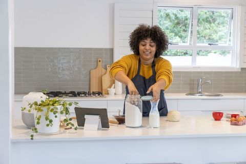 Home baker measuring flour from jar while following tablet recipe in bright modern kitchen