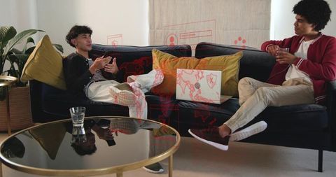 Young men relaxing on navy velvet sofa discussing laptop data and cybersecurity