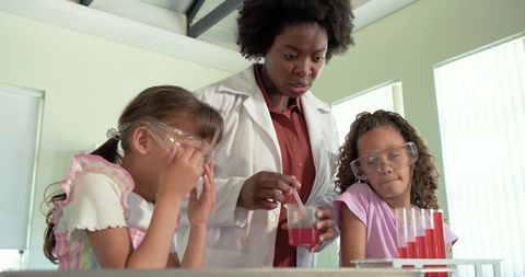 Stem instructor guiding two girls through hands-on chemistry experiment with safety goggles