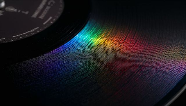 Macro vinyl grooves catching rainbow spectrum on glossy black lp for retro music design