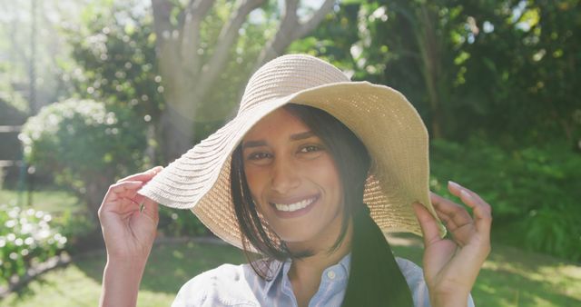 Young woman enjoying sunny day in garden, wearing straw hat. Suitable for use in lifestyle blogs, gardening websites, summer and fashion advertisements, and social media posts promoting outdoor activities.