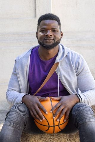 Urban basketball player sitting on stone steps holding ball in casual hoodie portrait