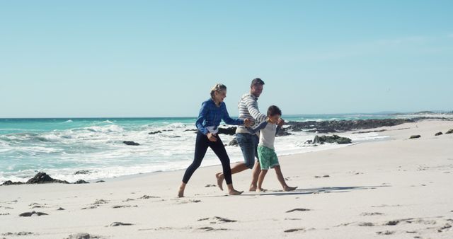 A cheerful family enjoying quality time together, walking barefoot on a sunny beach. The parents hold hands with their joyous child as they head towards the camera. Perfect imagery for vacation advertisements, family travel blogs, summer getaway promotions, or any marketing materials emphasizing quality family time and outdoor recreation.