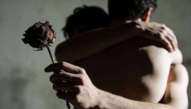 Two men embracing while holding wilted rose, intimate chiaroscuro couple portrait