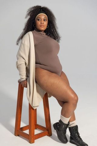 Confident african american plus-size model posing on stool in bodysuit and knit cardigan