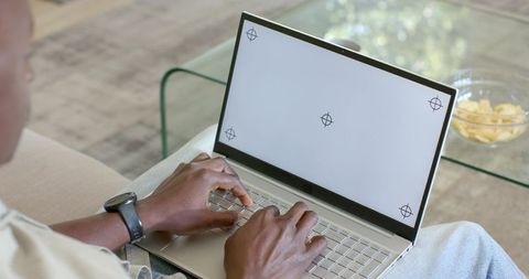 Mid-adult man typing on laptop on living room sofa with calibration crosshair screen