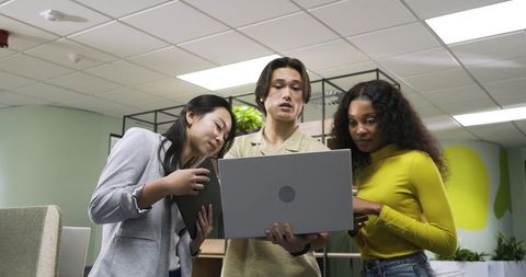 Diverse Coworkers Collaborating Over Laptop in Modern Office