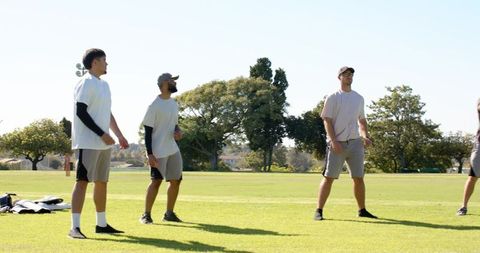 Male cricket team standing aligned on sunny practice field preparing for friendly match