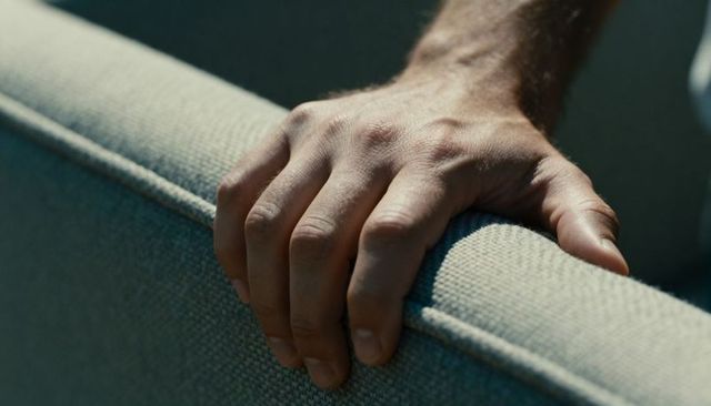 Male hand gripping sofa armrest closeup showing upholstery texture and tension
