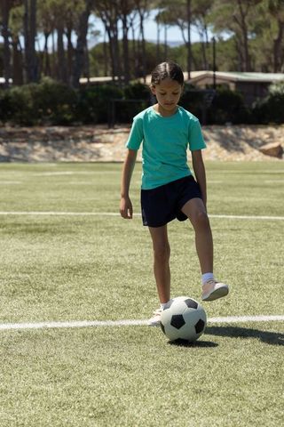 Young asian girl dribbling soccer ball on sunlit turf during youth practice and training