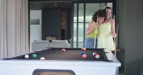 Friends hugging behind pool table in contemporary living room, casual home leisure