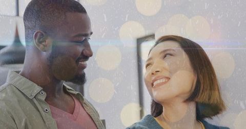 Smiling couple exchanging warm looks at home wearing casual layers intimate bokeh