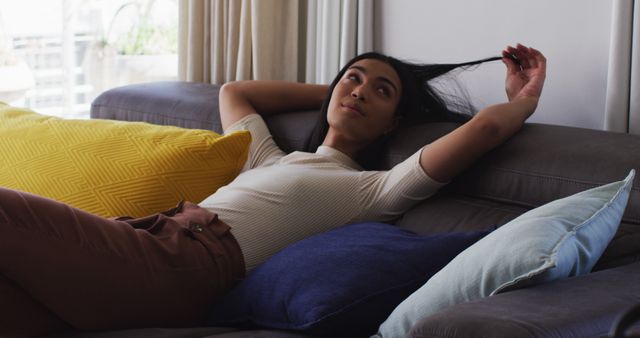 Young woman relaxing on sofa at home with bright pillows - Download Free Stock Images Pikwizard.com