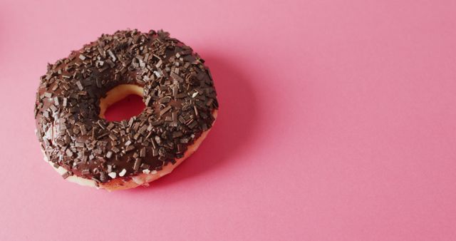 A delicious chocolate glazed donut covered with chocolate sprinkles sits captivatingly against a pink background. Ideal for bakery marketing, dessert blogs, social media posts on indulgent treats, or artistic food presentations.