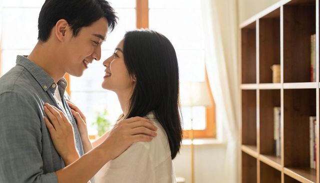Young couple sharing intimate gaze in sunlit living room, cozy romantic moment at home