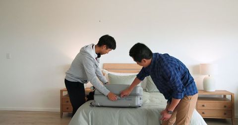 Father and son packing suitcase for family trip in bedroom