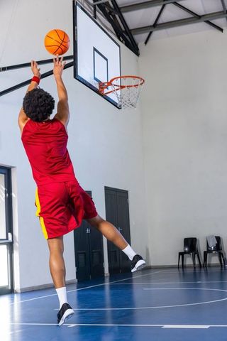 Basketball player jumping and shooting layup toward rim on indoor gym court
