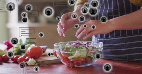 Tossing fresh garden salad with hands over glass bowl on red counter with social chat icons