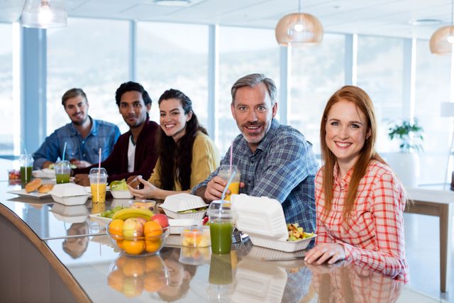 Group of colleagues enjoying a meal together in a modern office environment. Provides a casual and friendly atmosphere showcasing team bonding and workplace camaraderie. Ideal for illustrating concepts of teamwork, corporate culture, healthy eating in the workplace, and casual business meetings.