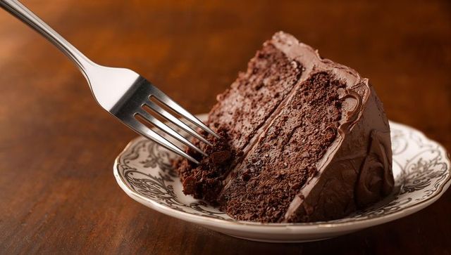 Fork pulling rich chocolate layer cake slice from ornate porcelain plate showing crumbs