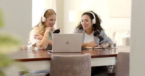 Two female hosts recording podcast with laptop and microphones
