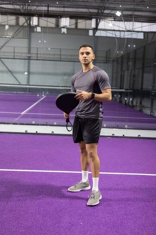 Male athlete standing on purple indoor court holding paddle preparing for competitive play