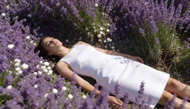 Woman relaxing in lavender field wearing sleeveless white dress, sunlit floral beauty